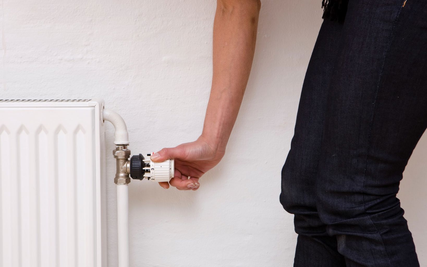 En hånd drejer på en termostat på en radiator