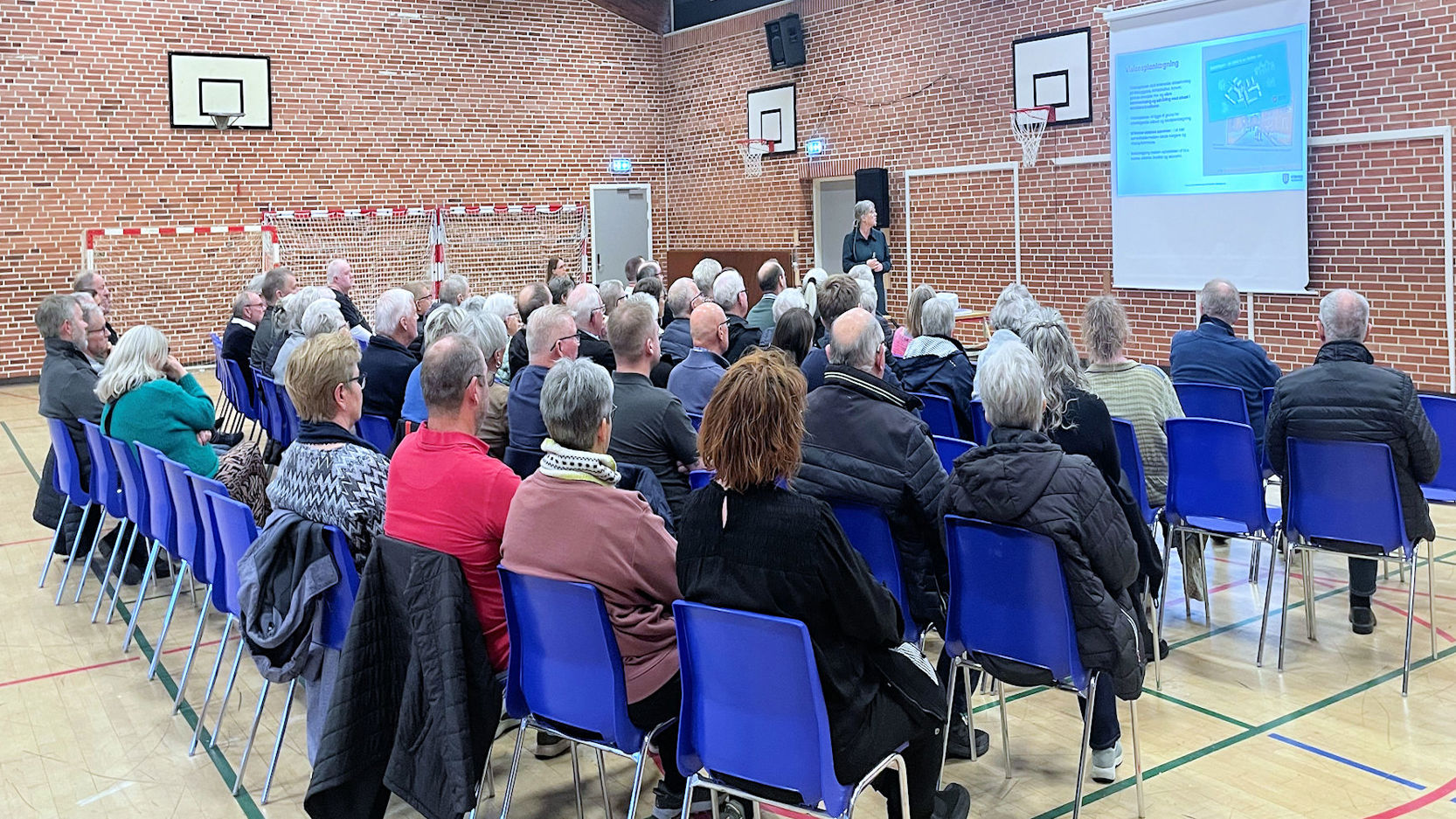 Voksne personer sidder i et lokale og lytter til oplægsholder