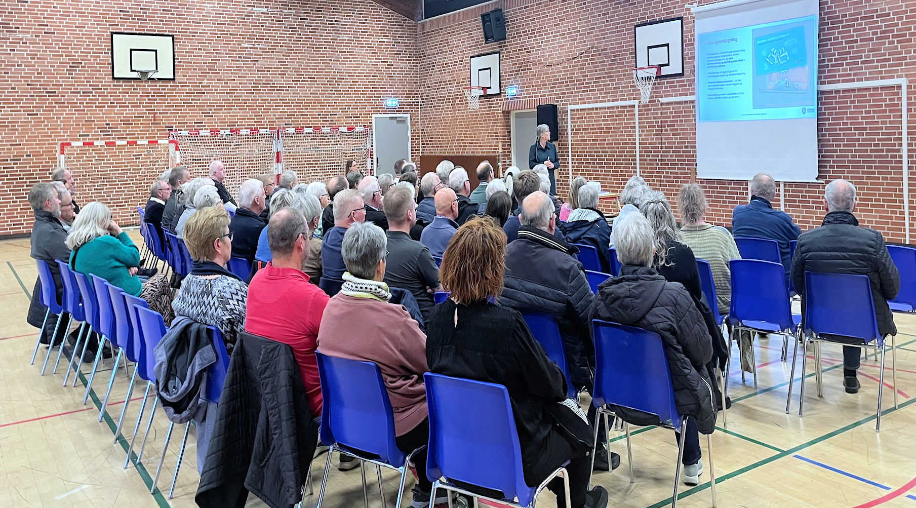 Voksne personer sidder i et lokale og lytter til oplægsholder