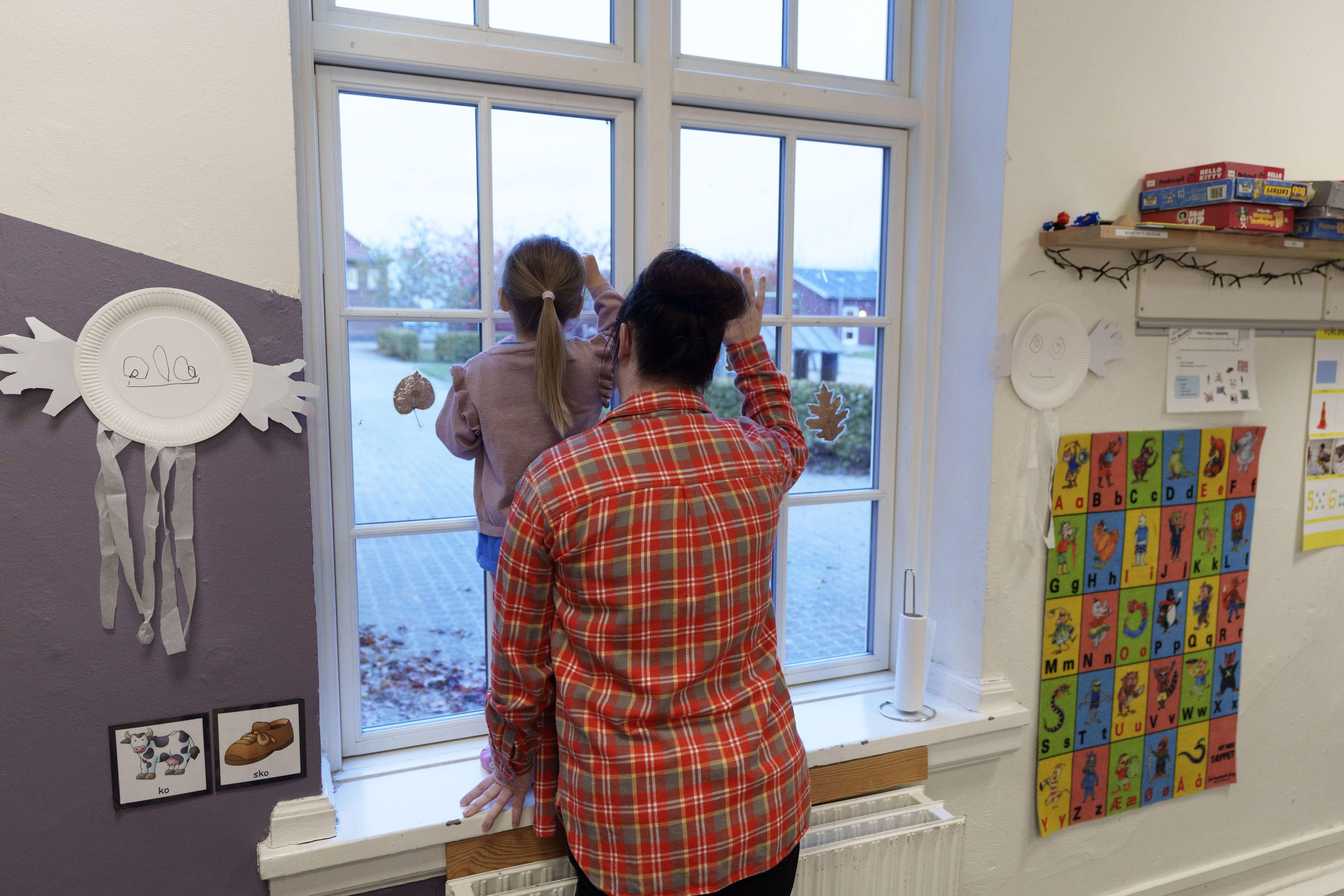 Pædagog og barn vinker farvel gennem vindue
