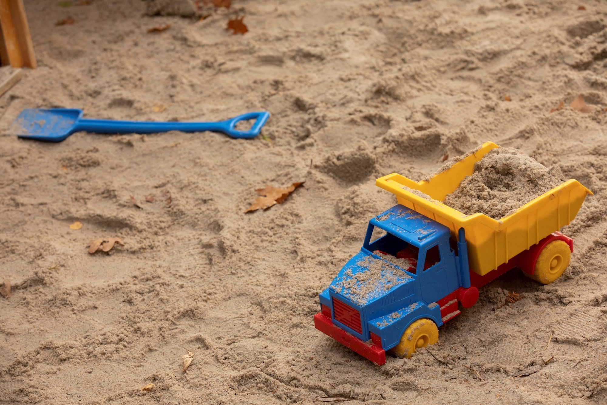 Legetøjslastbil og skovl, der ligger i sandkasse