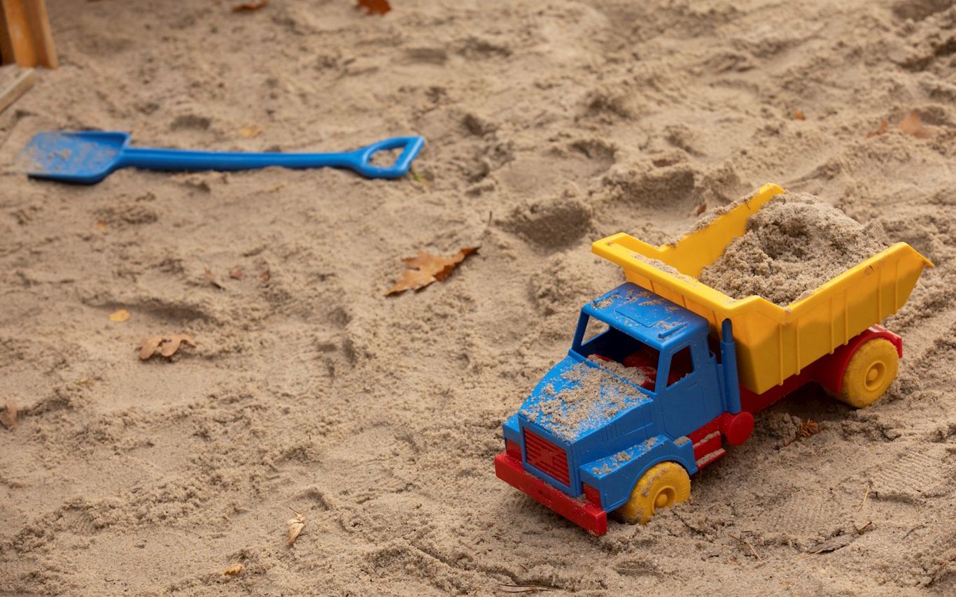 Legetøjslastbil og skovl, der ligger i sandkasse