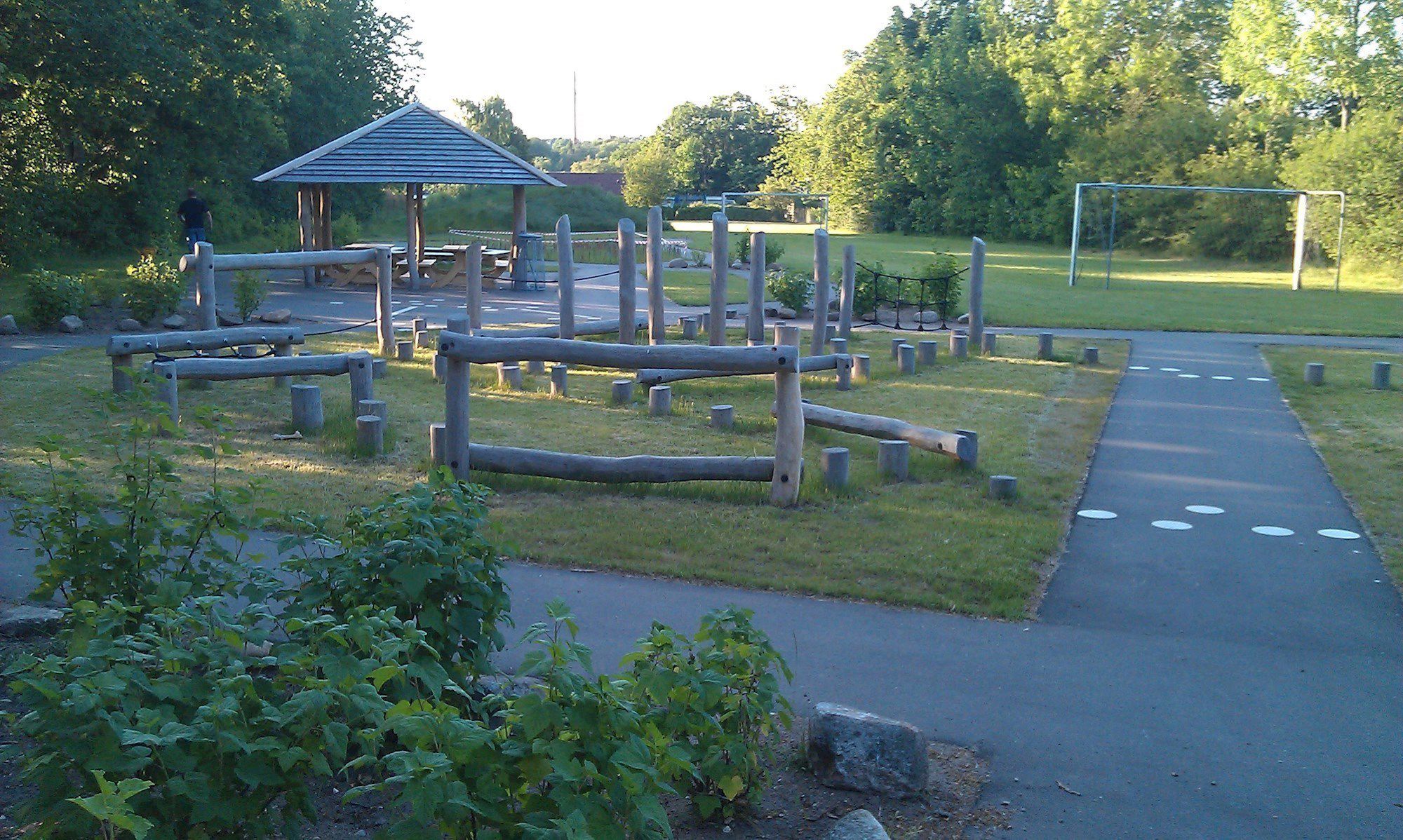 Legeplads med mange klatreredskaber i træ. Fodboldmål i baggrunden