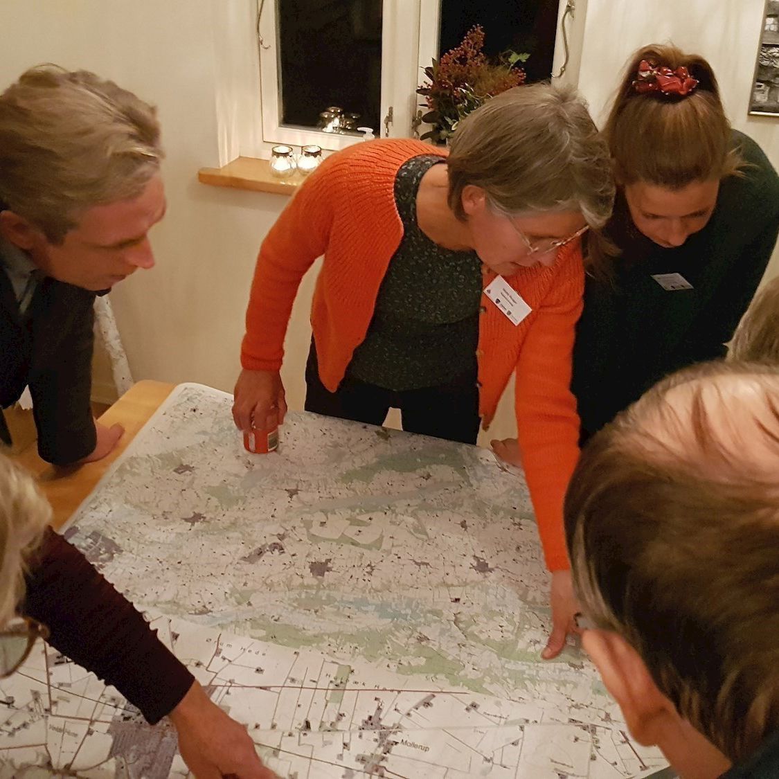 8 voksne samlet om et bord, hvorpå der ligger et kort